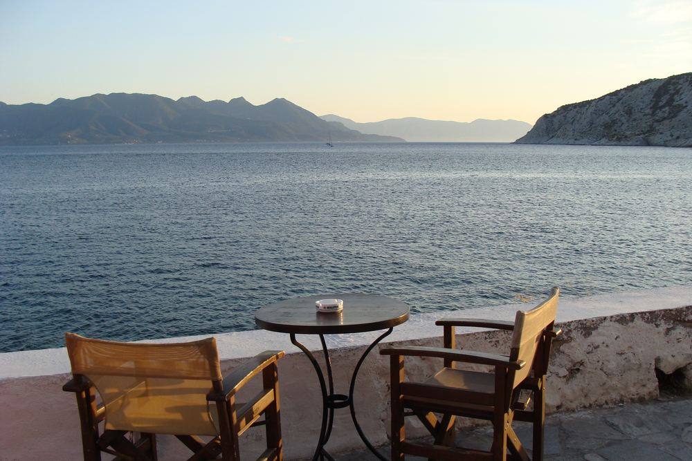 Empty taverna tables above the water at Perdika, Aegina, looking across the strait at dusk