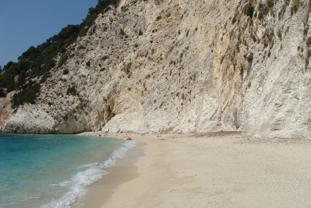 Pale cliffs falling into clear shallow water above an empty beach at Afales Bay, Ithaca