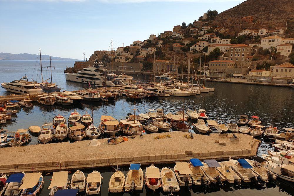 Fishing boats and yachts along the stone quay of Hydra harbor with the town rising behind