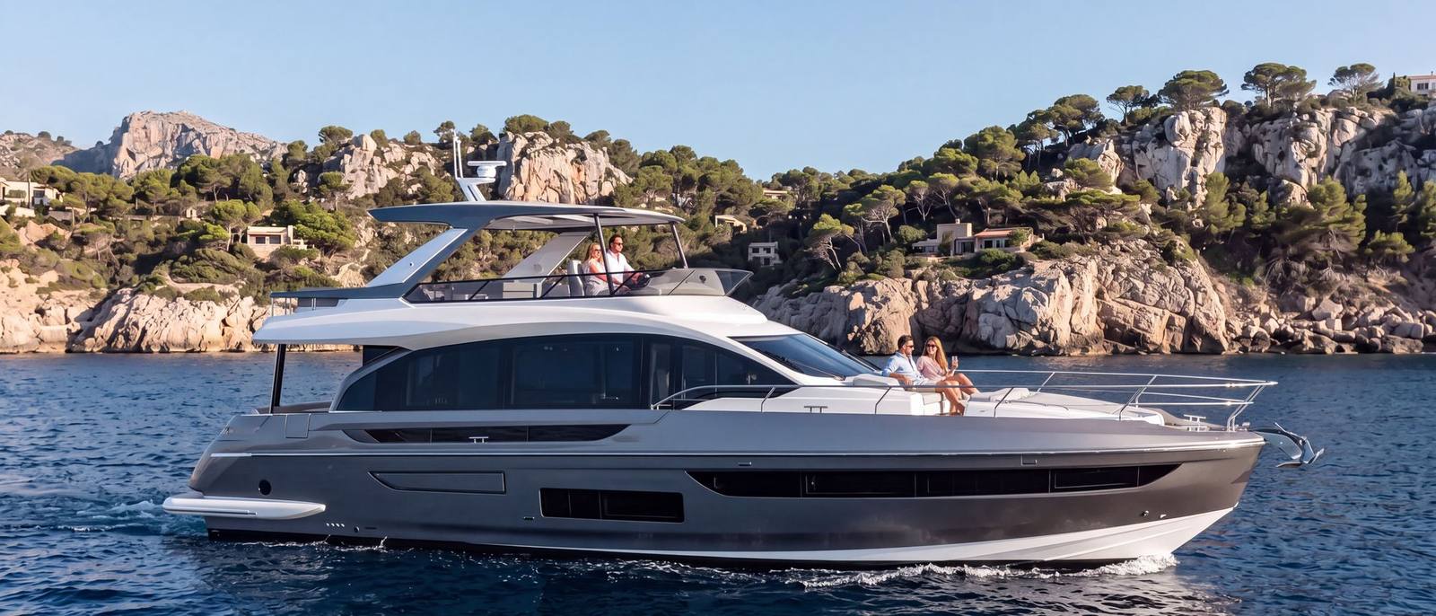 Flybridge Motor Yacht under way close to a pine-covered rocky Mediterranean shore