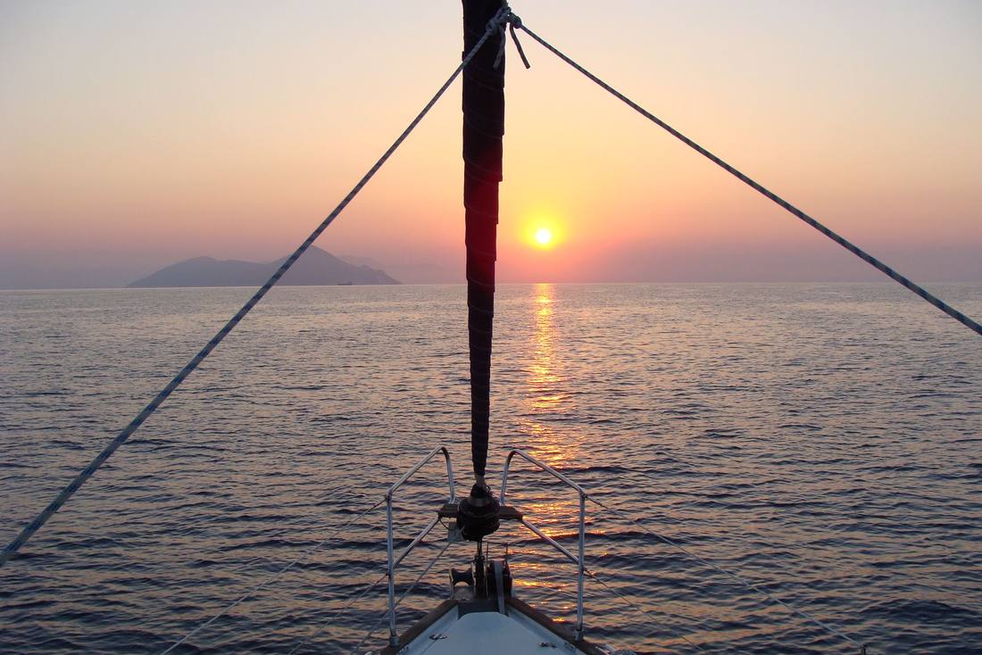 The sun going down over a low island seen from the bow of a Sailing Yacht under way